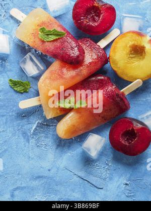 Vue rapprochée de prune et pêche popsicle sur fond de béton bleu. Crème glacée aux fruits popsicles avec des prunes fraîches et de la pêche. Copier l'espace Banque D'Images