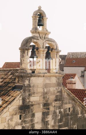 Trois cloches sur un vieux clocher en pierre sur un fond de toits de tuiles. Banque D'Images