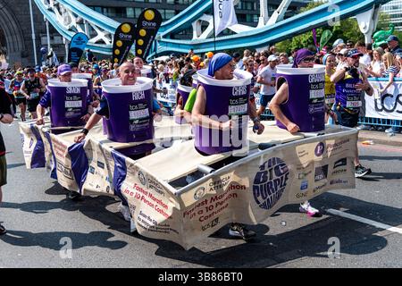 Dix personnes exécutant le Big Purple Challenge en costume de fantaisie pour le cancer du pancréas Royaume-Uni lors du marathon de Londres 2025 sur Tower Bridge, Londres, Royaume-Uni Banque D'Images