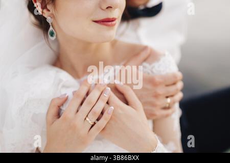 Le marié embrasse doucement la mariée de derrière sur leurs mains sont des anneaux de mariage. Banque D'Images