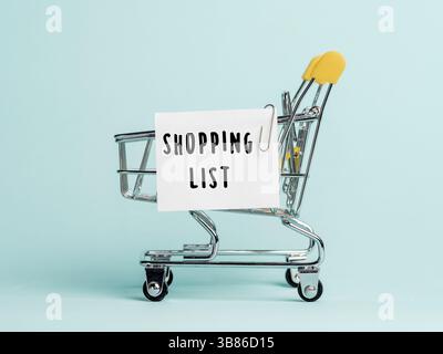 Panier d'achats et texte liste d'achats sur la liste de notes du livre blanc. Concept de liste d'achats sur fond bleu Banque D'Images