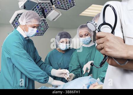 Médecin tenant un stéthoscope au-dessus de l'équipe des chirurgiens pendant une intervention chirurgicale Banque D'Images