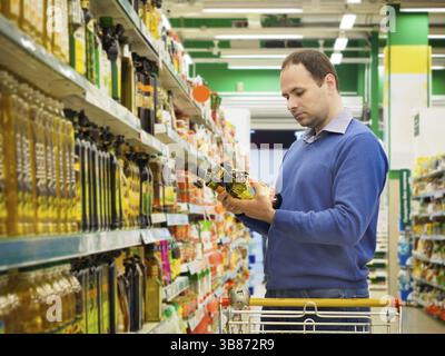 Man making choise sur deux bouteilles d'huile à partir de la tablette au supermarché. Le consumérisme concept Banque D'Images