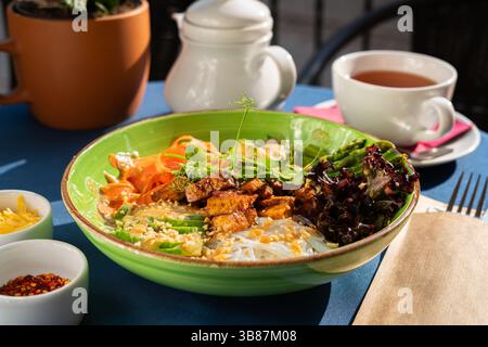 Nouilles de riz servies avec tofu, asperges, morceaux d'avocat, laitue rouge et morceaux d'arachides grillés. Servi dans un bol vert. Ensemble petit déjeuner Banque D'Images