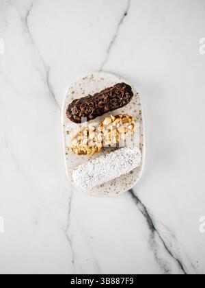 Ensemble de trois eclairs faits maison sur fond de marbre. Vue de dessus de délicieux profils sains avec différents éléments de décor - chocolat, cacahuètes et SH Banque D'Images