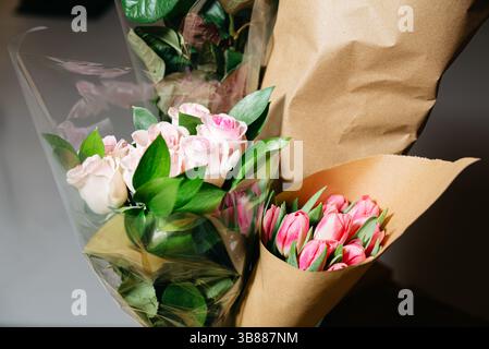 Gros plan de roses roses fraîches et de tulipes enveloppées dans du papier brun et transparent, créant un arrangement cadeau floral élégant pour les occasions spéciales. Banque D'Images