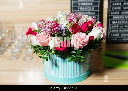 Un bel arrangement floral mettant en vedette des roses et le souffle de bébé dans un élégant coffret cadeau rayé, affiché sur une surface en bois avec de la verrerie. Banque D'Images