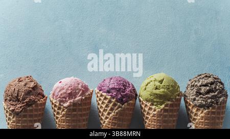 Diverses boules de glace dans des cônes avec copie espace. La crème glacée dans des cônes de couleur chocolat, fraise, myrtille, pistache ou matcha, biscuits chocola Banque D'Images
