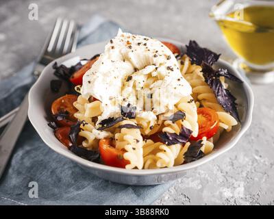 Savoureuses pâtes italiennes fusilli avec cerise, mozarella ou buratta et basilic frais. Plat avec des pâtes sur fond de béton gris. Copier l'espace. En bonne santé Banque D'Images