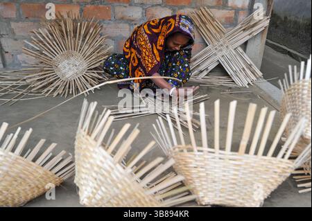 23 janvier 2024 : une femme tisse des produits fabriqués à partir de cannes de bambou à Haripur, dans le quartier de Nomshuddha à la périphérie de Sylhet, au Bangladesh. Ils vendent vingt paniers à des négociants locaux à un prix de gros de 600 TK. Depuis un siècle et demi, environ 60 familles de ce village sont impliquées dans le tissage de produits artisanaux en rotin pour générer des revenus supplémentaires pour leurs familles. Avec l'augmentation des produits ménagers en plastique qui prennent le dessus sur le marché, les artisans se retirent de plus en plus de l'industrie de la canne de bambou naturelle. Maintenant, certaines de ces personnes font encore peu de travail juste Banque D'Images