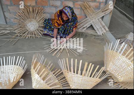 23 janvier 2024 : une femme tisse des produits fabriqués à partir de cannes de bambou à Haripur, dans le quartier de Nomshuddha à la périphérie de Sylhet, au Bangladesh. Ils vendent vingt paniers à des négociants locaux à un prix de gros de 600 TK. Depuis un siècle et demi, environ 60 familles de ce village sont impliquées dans le tissage de produits artisanaux en rotin pour générer des revenus supplémentaires pour leurs familles. Avec l'augmentation des produits ménagers en plastique qui prennent le dessus sur le marché, les artisans se retirent de plus en plus de l'industrie de la canne de bambou naturelle. Maintenant, certaines de ces personnes font encore peu de travail juste Banque D'Images