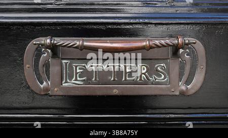 Ancienne poignée de porte de boîte aux lettres en métal victorien ornée vintage sur porte noire Banque D'Images