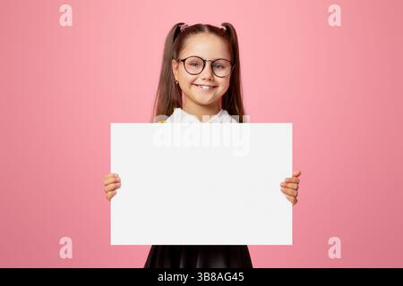 Gaie enfant écolière en uniforme et verres tient l'affiche avec espace vide Banque D'Images