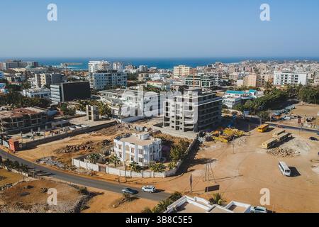 Une vue aérienne de Ngor, Dakar, montre un chantier de construction avec des grues et des bus près d'une villa blanche. Le paysage urbain s'étend à l'océan, avec moderne Banque D'Images