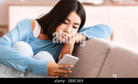Une dame frustrée qui vérifie le téléphone portable assis sur le canapé Banque D'Images
