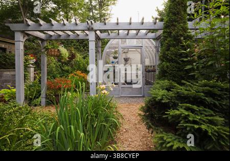 Chemin du paillis de cèdre bordé de fleurs d'Iris « drapeau jaune », Picea Abies nidiformis - épinette de nid d'oiseau, arbres Thuja occidentalis menant à la serre. Banque D'Images