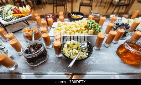Petit déjeuner coloré ou table de brunch buffet avec assortiment de fromages, fruits frais, fruits secs, mini smoothies dans des verres à dose, confitures, et miel, tout beau Banque D'Images