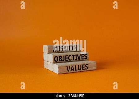 Symbole des valeurs des objectifs de mission. Mots conceptuels objectifs de mission valeurs sur blocs de bois. Beau fond orange. Affaires et Mission objectiv Banque D'Images