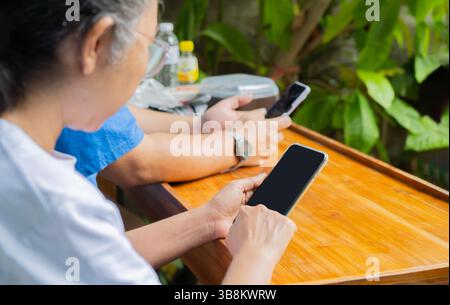 Image recadrée de la main tenant le téléphone portable avec l'écran noir blanc dans le café vintage et l'homme asiatique flou assis à proximité en arrière-plan Banque D'Images