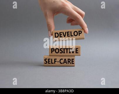 Développez un symbole d'autosoins positif. Les mots conceptuels développent un autosoin positif sur les blocs de bois. Beau fond gris. Main d'homme d'affaires. Business an Banque D'Images