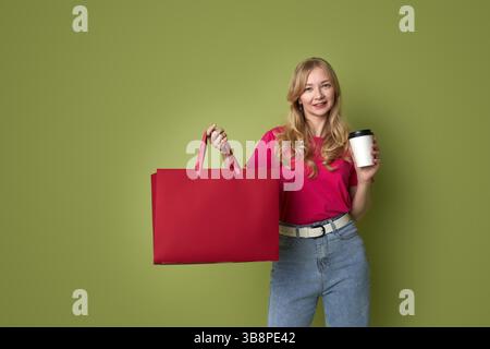 Jeune femme élégante tenant du café et des sacs à provisions sur fond vert Banque D'Images