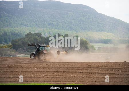 Tracteur utilisant un rouleau ou un cultipacker sur un champ près d'Aviemore en Écosse créant un nuage de poussière d'érosion du sol Banque D'Images