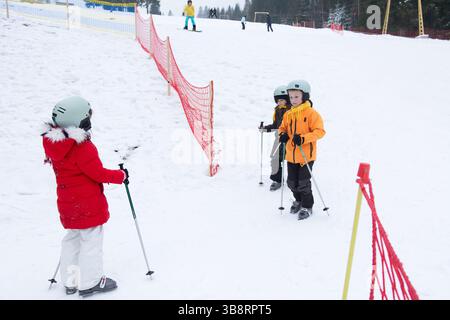 Les collines enneigées créent un pays des merveilles hivernales alors que les enfants se préparent à des leçons de ski, remplies de rires, de plaisir et de camaraderie dans un ensemble enneigé serein Banque D'Images
