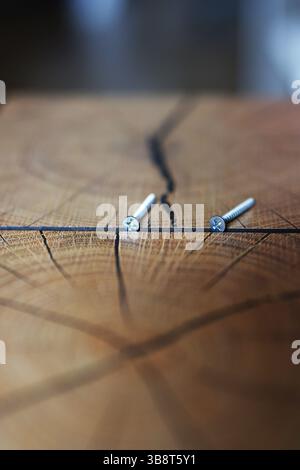 Gros plan de deux vis métalliques sur une surface en bois fissurée, symbolisant le bricolage, la menuiserie ou les travaux de réparation en mettant l'accent sur la texture et l'artisanat. Banque D'Images