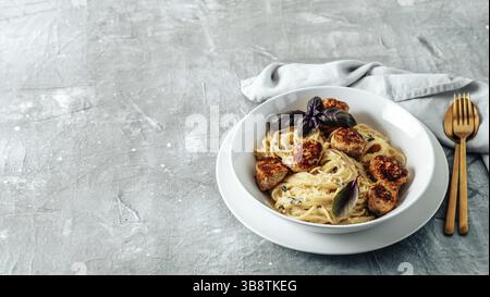 Boulettes de parmesan de courgettes aux pâtes Carbonara dans une assiette blanche sur fond gris. Vue rapprochée de la carbonara crémeuse avec espace de copie restant Banque D'Images