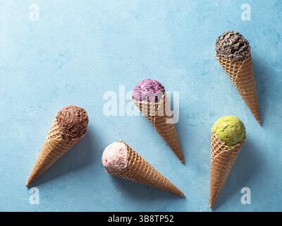 Diverses boules de glace dans des cônes avec copie espace. La crème glacée dans des cônes de couleur chocolat, fraise, myrtille, pistache ou matcha, biscuits chocola Banque D'Images
