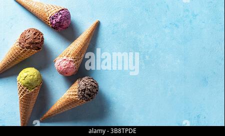 Diverses boules de glace dans des cônes avec copie espace. La crème glacée dans des cônes de couleur chocolat, fraise, myrtille, pistache ou matcha, biscuits chocola Banque D'Images