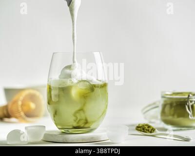 Thé glacé au Matcha Latte avec crème fouettée versée dans un verre à gobelet. Matcha latte et ingrédients sur fond de marbre blanc. Espace de copie pour txt ou desi Banque D'Images