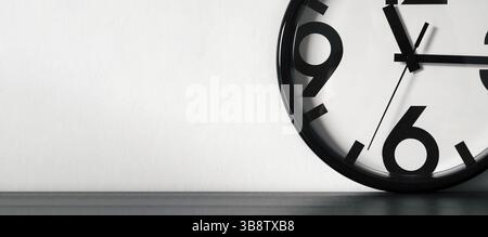Horloge minimaliste moderne ou simple blanc et noir sur table en bois noir et mur blanc avec espace pour le texte. Longue bannière horizontale Banque D'Images