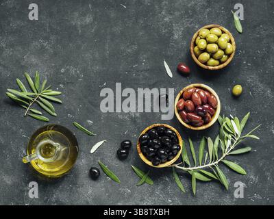 Ensemble d'olives vertes, noires et rouges ou roses et d'huile d'olive sur fond sombre. Différents types d'olives dans des bols en bois d'olive et de l'huile d'olive sur c foncé Banque D'Images