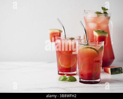 Refroidisseur de pastèque avec citron vert, menthe et glace. Parfait boisson maison de pastèque dans des verres avec pailles en métal sur fond blanc, espace de copie restant pour le tex Banque D'Images