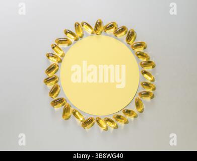 Capsules liquides de vitamine D3 autour du cercle jaune sur fond gris neutre. Vue de dessus ou soleil jaune plat fait avec cercle de papier et capsules liquides Banque D'Images