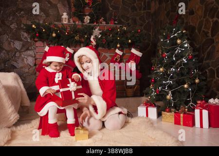 Mère et fille sont assis près de la cheminée et arbre de noël avec des boîtes-cadeaux Banque D'Images