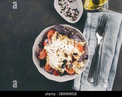 Fusillis italienne avec cherry, de la mozzarella buratta ou le fromage et le basilic. Plat avec des pâtes sur fond de béton noir. Vue d'en haut. Spa de copie Banque D'Images