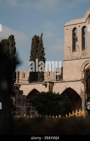 Ruines de l'abbaye de Bellapais à Chypre avec des cyprès et des arches en pierre gothique sous la lumière douce du matin. Banque D'Images