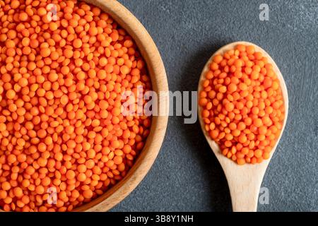 Grains de lentilles rouges dans un bol en bois et cuillère sur fond gris. Vue de dessus des lentilles orange séchées à l'intérieur du bol. Banque D'Images