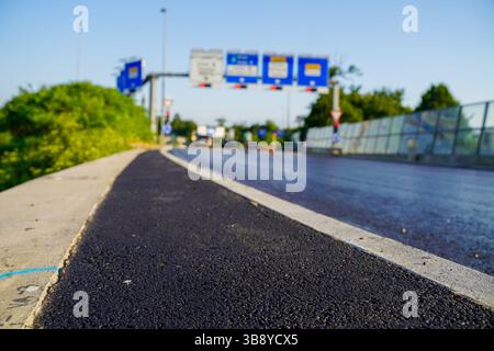 Bretelle d'autoroute fraîche menant au rond-point avec de nouveaux marquages routiers, feux de circulation et panneaux Banque D'Images