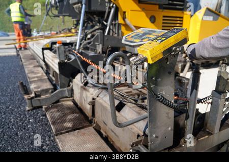 Chape de revêtement en asphalte en action, pose d'asphalte frais avec panneau de commande visible, mettant en valeur le processus de revêtement et les machines sur une construction de route Banque D'Images