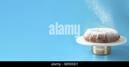 Sucre glace tombant de gâteau de petit pain frais fait maison. Le sucre en poudre tombe sur le gâteau frais sur fond bleu. Copier l'espace pour le texte. Idées et recettes Banque D'Images