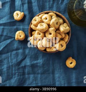 Taralli ou taralini italien traditionnel dans un bol en bois sur fond de serviette bleu foncé. Photo rustique de taralli apéritif avec espace copie Banque D'Images