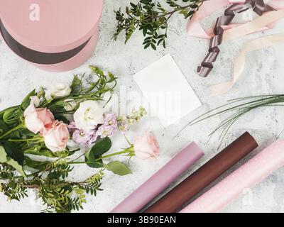 Pose à plat floristique. Fleurs, papier d'emballage, boîte-cadeau et carte vide blanche sur le dessus de table gris. Copier l'espace Banque D'Images