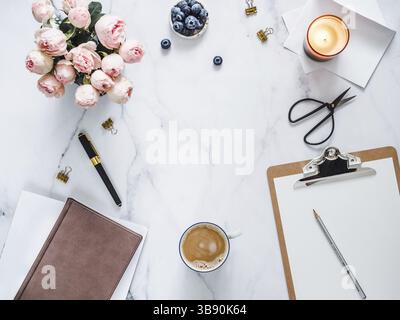 Vue de dessus du bureau à domicile des femmes avec espace de copie au centre. Presse-papiers, fleurs, bougie parfumée sur marbre blanc. Maquette de bureau féminine avec copie s. Banque D'Images