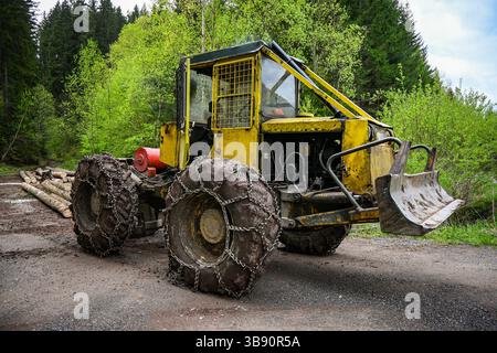 Débardeur jaune avec chaînes antidérapantes est garé sur un chemin de terre dans une forêt, prêt pour la récolte de bois. Banque D'Images