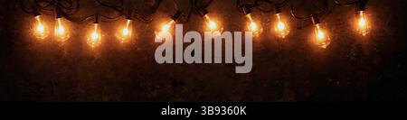 Rangée de guirlande lumineuse lumineuse sur fond sombre et grundy. Banque D'Images