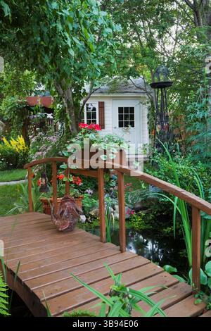 Surplombant Malus 'Liberty' - feuilles de pommier sur une passerelle en bois brun décorée de pélargonium rouge - fleurs de géranium menant au jardin blanc Banque D'Images