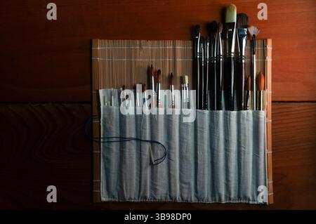 Un assortiment de pinceaux d'artiste dans un organisateur en bambou sur des planchers de bois. Banque D'Images